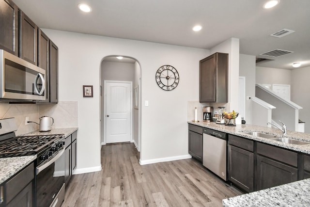 2832 Madison Dr, Conroe, TX 77304 - kitchen featuring stainless steel appliances, arched walkways, light wood-type flooring, dark brown cabinetry, and light stone counters