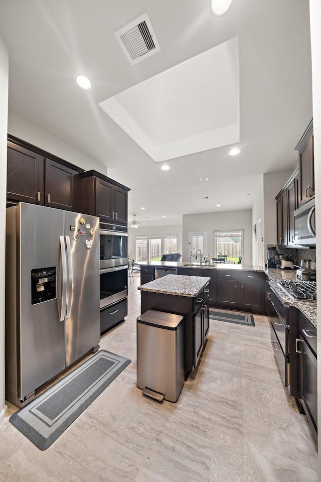 5442 Atwood Canyon Ct, Richmond, TX 77407 - kitchen with appliances with stainless steel finishes, a tray ceiling, light stone counters, recessed lighting, and dark brown cabinetry