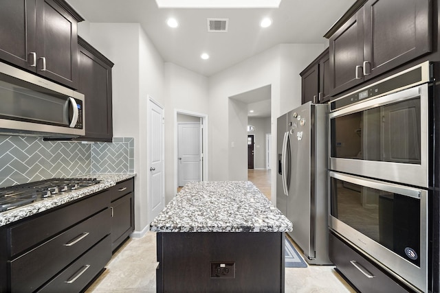 5442 Atwood Canyon Ct, Richmond, TX 77407 - kitchen with appliances with stainless steel finishes, a center island, light stone countertops, dark brown cabinetry, and tasteful backsplash
