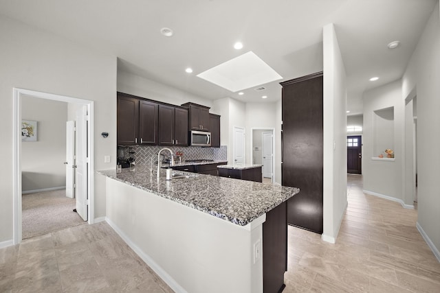5442 Atwood Canyon Ct, Richmond, TX 77407 - kitchen featuring stainless steel microwave, a skylight, dark brown cabinetry, light stone countertops, and a kitchen island