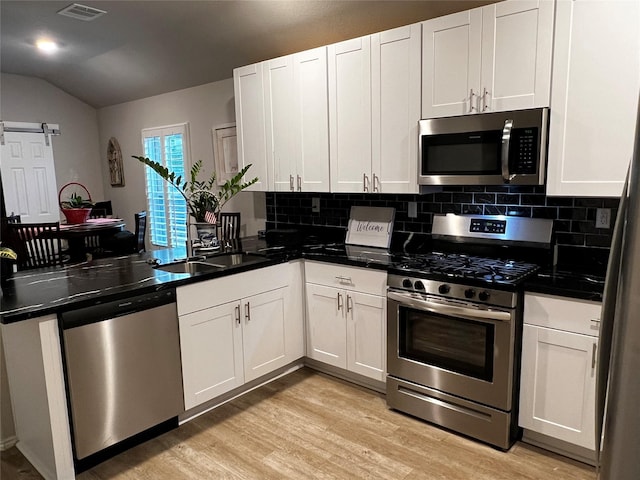 278 Cumberland Forest Dr, Magnolia, TX 77354 - kitchen featuring appliances with stainless steel finishes, a peninsula, tasteful backsplash, vaulted ceiling, and light wood finished floors