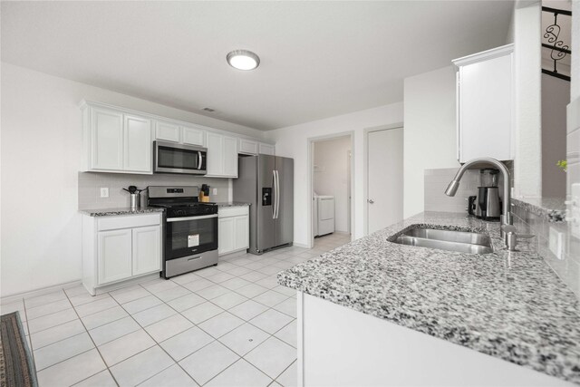 5767 Wandering Creek Dr, Richmond, TX 77469 - kitchen with appliances with stainless steel finishes, decorative backsplash, washing machine and clothes dryer, white cabinetry, and light stone counters