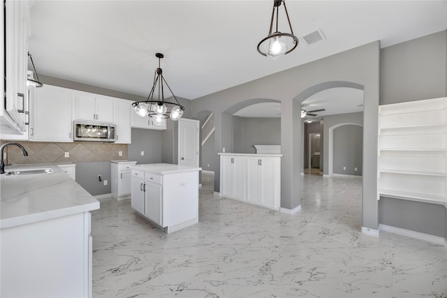537 Green Cedar Dr, League City, TX 77573 - kitchen with stainless steel microwave, arched walkways, backsplash, light marble finish flooring, and a ceiling fan