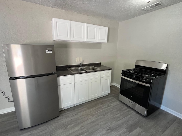 4831 Sycamore Ave Unit 16, Pasadena, TX 77503 - kitchen with stainless steel appliances, dark wood-style floors, dark countertops, white cabinetry, and a textured ceiling