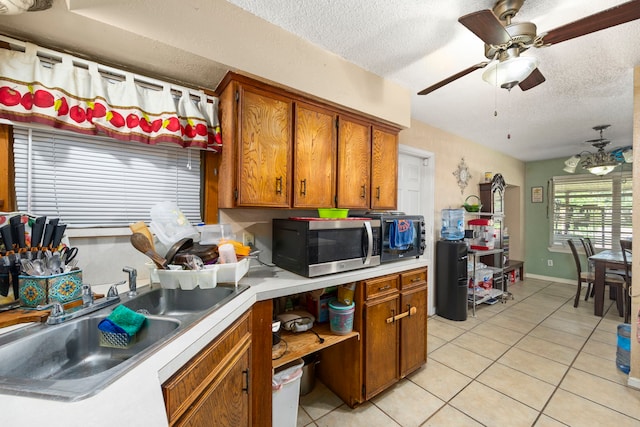 12337 Kayla Ln, Houston, TX 77015 - kitchen featuring stainless steel microwave, brown cabinetry, a textured ceiling, light tile patterned floors, and light countertops