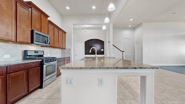 2135 Llerena Ln, League City, TX 77573 - kitchen with stainless steel appliances, arched walkways, light stone counters, decorative backsplash, and a center island with sink