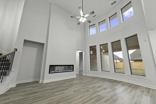 3232 Stingray Cove Dr, Katy, TX 77493 - unfurnished living room featuring a high ceiling, wood finished floors, stairway, a glass covered fireplace, and a ceiling fan