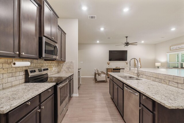26410 Yaupon Crk, Magnolia, TX 77355 - kitchen with stainless steel appliances, tasteful backsplash, dark brown cabinetry, open floor plan, and light wood finished floors