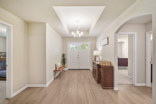 26410 Yaupon Crk, Magnolia, TX 77355 - foyer entrance featuring light wood-style flooring, arched walkways, a chandelier, and a tray ceiling