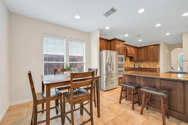 2513 Garnetfield Ln, Friendswood, TX 77546 - kitchen with stainless steel appliances, arched walkways, decorative backsplash, light tile patterned floors, and dark stone counters