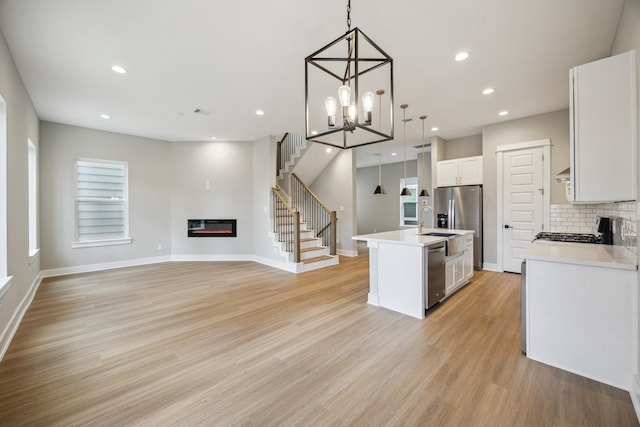 812 Thornton St Unit D, Houston, TX 77018 - kitchen featuring stainless steel appliances, a glass covered fireplace, a center island with sink, white cabinetry, and light wood-type flooring