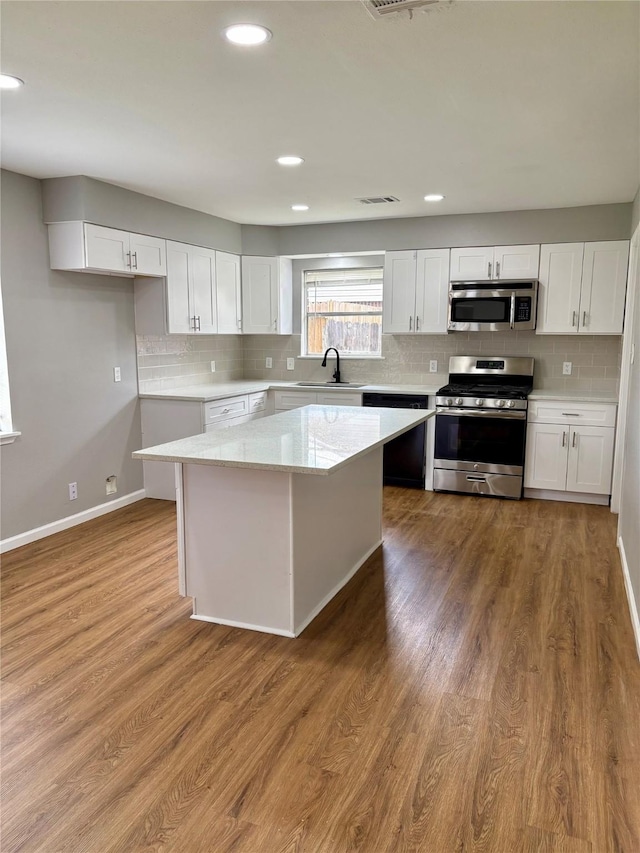 10434 Rocky Hollow Rd, La Porte, TX 77571 - kitchen with stainless steel appliances, white cabinets, backsplash, a kitchen island, and wood finished floors