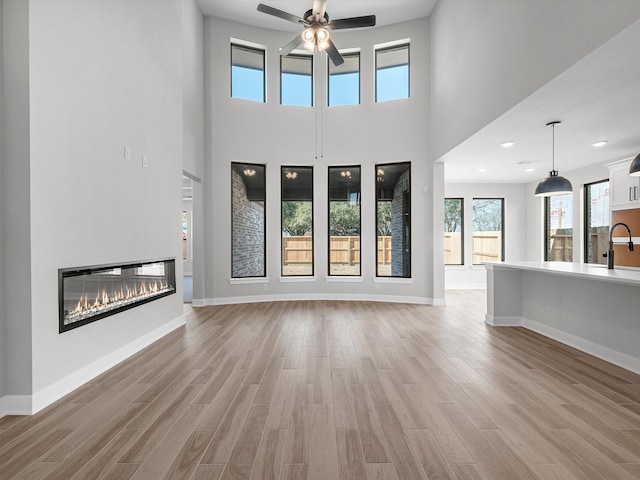 3185 Stingray Cove Dr, Katy, TX 77493 - unfurnished living room featuring a glass covered fireplace, light wood-style floors, a ceiling fan, and a towering ceiling