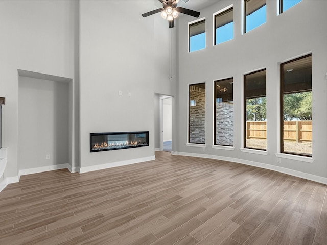 3185 Stingray Cove Dr, Katy, TX 77493 - unfurnished living room with a towering ceiling, a glass covered fireplace, a ceiling fan, and wood finished floors