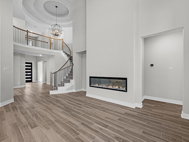 3185 Stingray Cove Dr, Katy, TX 77493 - unfurnished living room with a towering ceiling, stairway, wood finished floors, a glass covered fireplace, and a chandelier