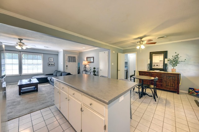 204 Meadow Ln, Brenham, TX 77833 - kitchen with ceiling fan, light tile patterned floors, white cabinetry, a center island, and crown molding