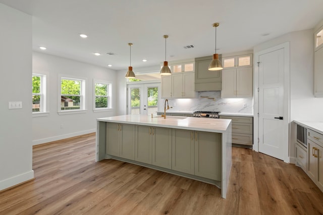 3224 Omega St, Houston, TX 77022 - kitchen featuring light wood-style floors, tasteful backsplash, a kitchen island with sink, recessed lighting, and glass insert cabinets