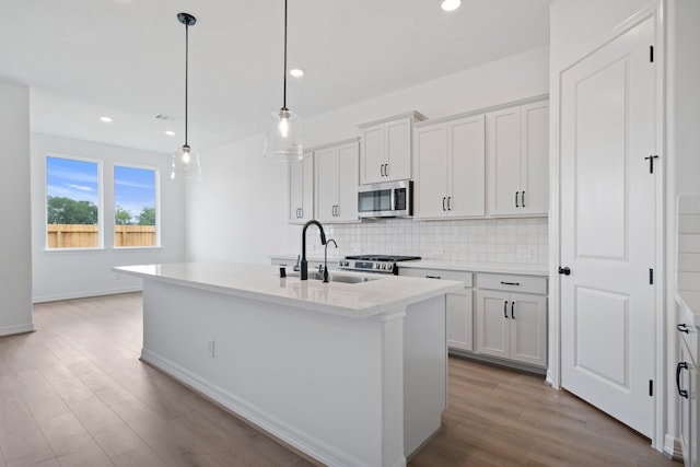 4770 Ara Dr, Richmond, TX 77469 - kitchen featuring stainless steel microwave, backsplash, light wood-type flooring, an island with sink, and white cabinetry