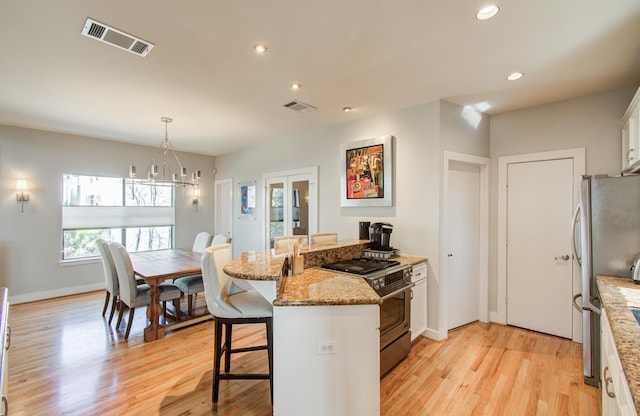 6205 Dell St, Houston, TX 77007 - kitchen featuring appliances with stainless steel finishes, a peninsula, white cabinetry, a breakfast bar, and a chandelier