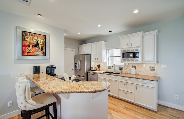 6205 Dell St, Houston, TX 77007 - kitchen with appliances with stainless steel finishes, backsplash, a breakfast bar area, white cabinetry, and light wood-type flooring