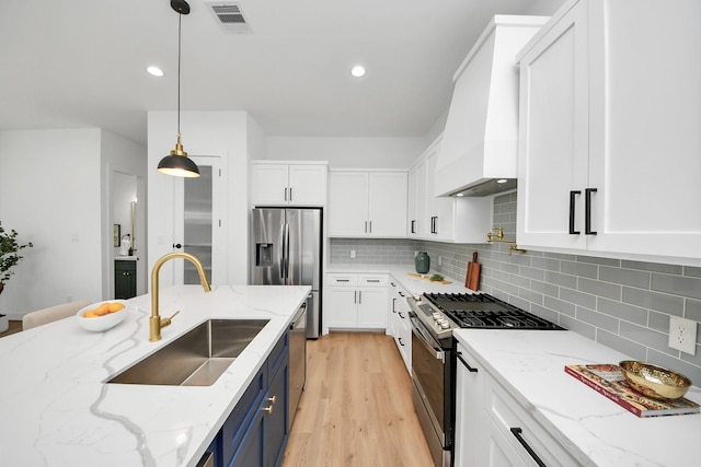 5520 Chapman St, Houston, TX 77009 - kitchen featuring appliances with stainless steel finishes, custom range hood, blue cabinets, white cabinets, and recessed lighting