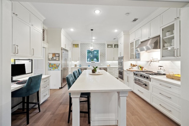 8703 Chelmsford Ln, Spring, TX 77379 - kitchen with range hood, appliances with stainless steel finishes, a breakfast bar area, recessed lighting, and white cabinets