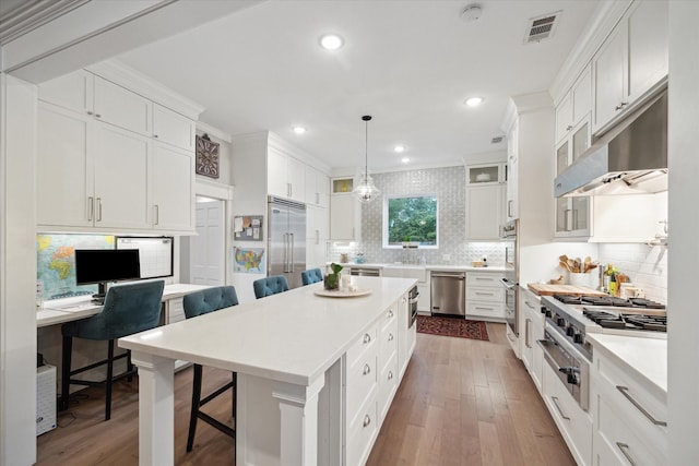 8703 Chelmsford Ln, Spring, TX 77379 - kitchen featuring stainless steel appliances, a kitchen breakfast bar, decorative backsplash, wood-type flooring, and white cabinets