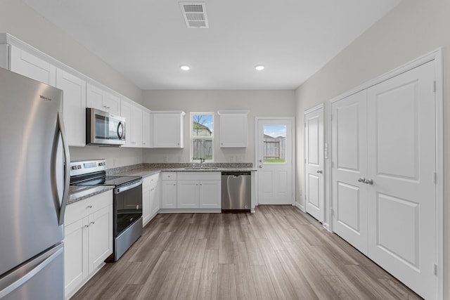 9309 Beryl Ln, Conroe, TX 77303 - kitchen with stainless steel appliances, wood finished floors, white cabinetry, recessed lighting, and light stone countertops