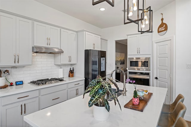 18427 Counce Meadow Ct, Cypress, TX 77433 - kitchen featuring stainless steel appliances, under cabinet range hood, backsplash, hanging light fixtures, and a kitchen bar