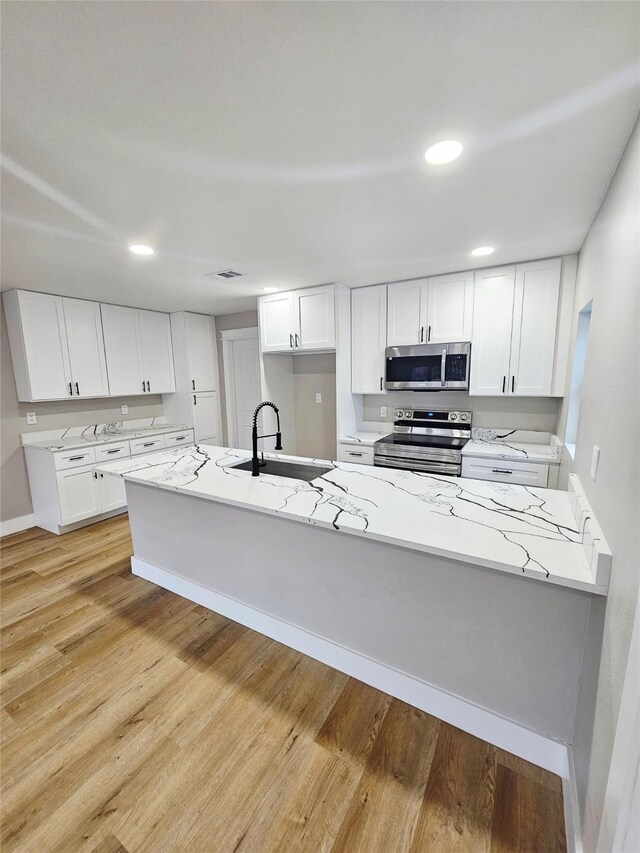 5014 Middleton St, Baytown, TX 77520 - kitchen with appliances with stainless steel finishes, light wood-type flooring, white cabinets, light stone countertops, and recessed lighting
