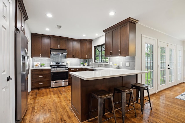 4614 Kinglet St, Houston, TX 77035 - kitchen with appliances with stainless steel finishes, under cabinet range hood, a peninsula, dark brown cabinetry, and wood finished floors