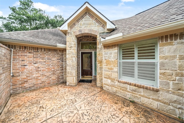 47 Dresden Pl, The Woodlands, TX 77382 - view of exterior entry with roof with shingles, brick siding, stone siding, and a patio area