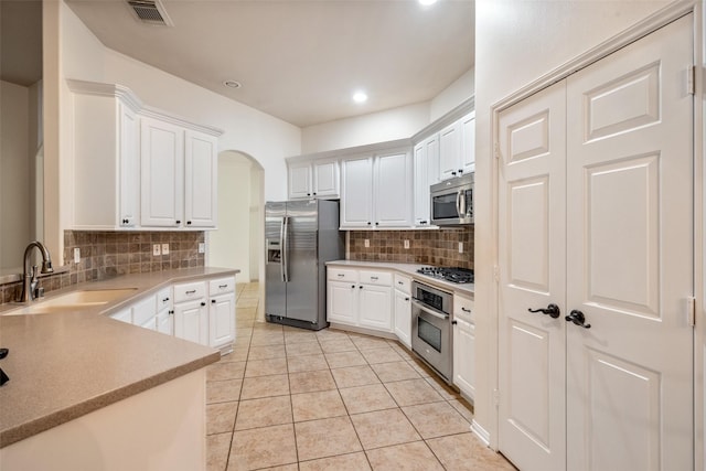 47 Dresden Pl, The Woodlands, TX 77382 - kitchen featuring stainless steel appliances, backsplash, white cabinetry, arched walkways, and light tile patterned floors