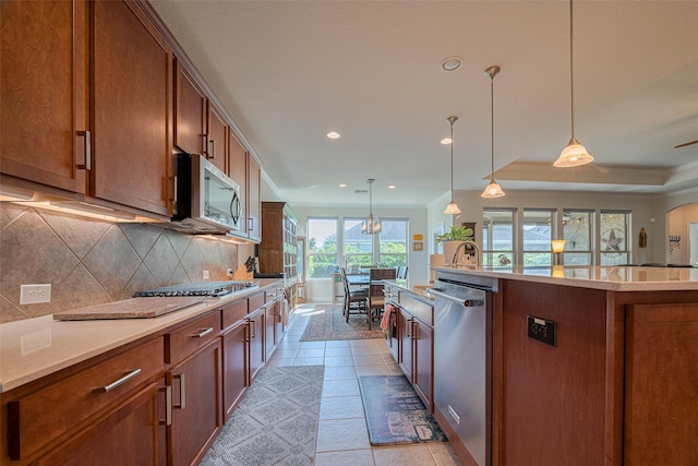 3903 Grand Fir Ct, Richmond, TX 77469 - kitchen featuring stainless steel appliances, backsplash, a center island with sink, brown cabinets, and hanging light fixtures