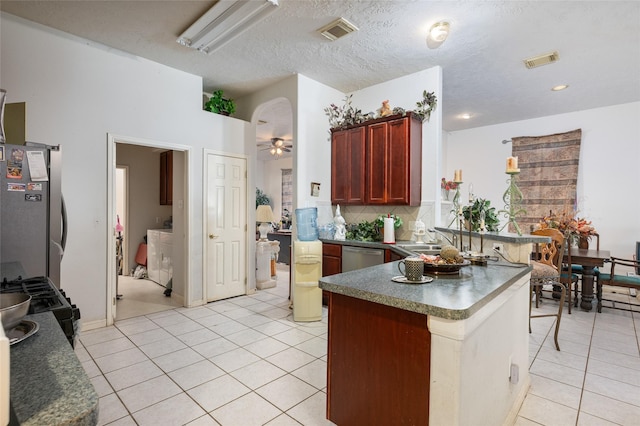 13703 Naples Park Ln, Houston, TX 77070 - kitchen featuring appliances with stainless steel finishes, reddish brown cabinets, dark countertops, light tile patterned floors, and a peninsula