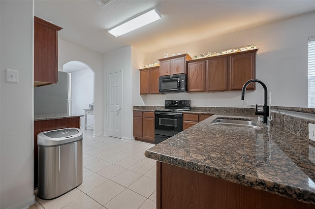 30914 Sweetwater Cir, Magnolia, TX 77355 - kitchen with black appliances, arched walkways, light tile patterned floors, dark stone counters, and a peninsula