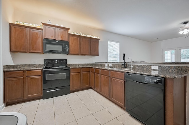 30914 Sweetwater Cir, Magnolia, TX 77355 - kitchen featuring black appliances, a peninsula, light tile patterned floors, dark stone countertops, and brown cabinets