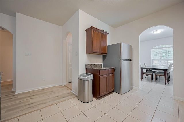 30914 Sweetwater Cir, Magnolia, TX 77355 - kitchen with freestanding refrigerator, arched walkways, dark stone countertops, brown cabinetry, and light tile patterned flooring