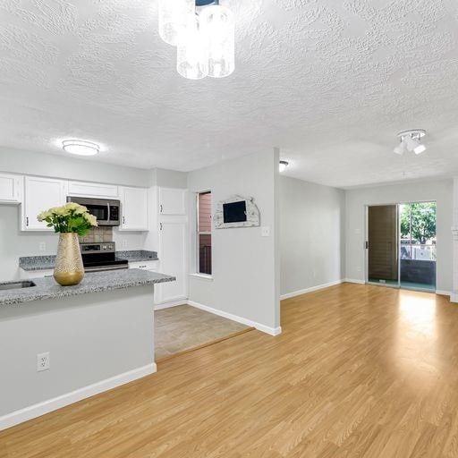 10555 Turtlewood Ct Unit 1803, Houston, TX 77072 - kitchen featuring appliances with stainless steel finishes, white cabinetry, a textured ceiling, light wood-style flooring, and a chandelier