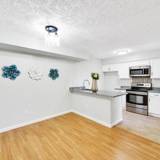 10555 Turtlewood Ct Unit 1803, Houston, TX 77072 - kitchen with stainless steel appliances, white cabinetry, a peninsula, a textured ceiling, and light wood finished floors