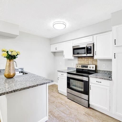 10555 Turtlewood Ct Unit 1803, Houston, TX 77072 - kitchen with stainless steel appliances, light stone counters, white cabinetry, backsplash, and a textured ceiling