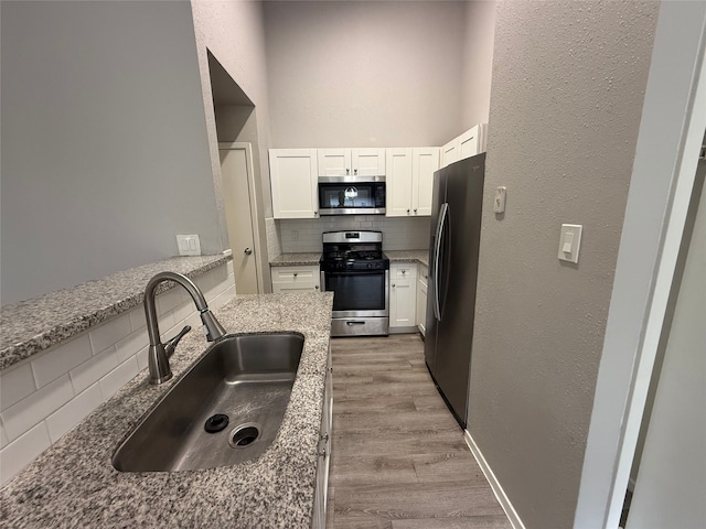 10052 Sharpton Dr, Houston, TX 77038 - kitchen featuring appliances with stainless steel finishes, backsplash, white cabinets, light wood finished floors, and light stone counters