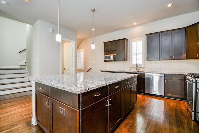 1909 Hickory St, Houston, TX 77007 - kitchen featuring appliances with stainless steel finishes, dark wood-type flooring, decorative backsplash, a center island, and dark brown cabinetry