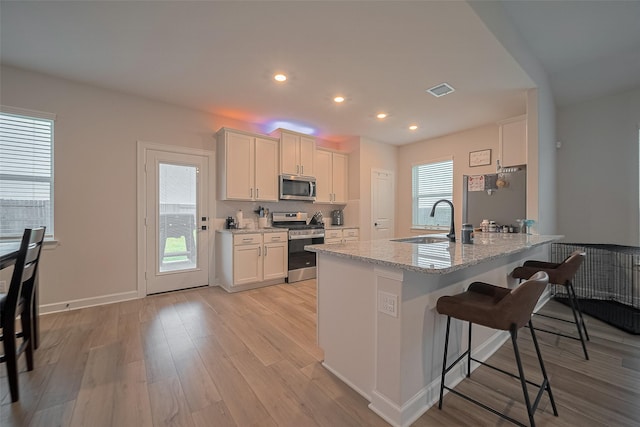 3213 Overfalls Dr, Santa Fe, TX 77510 - kitchen with appliances with stainless steel finishes, a kitchen bar, light wood-style floors, recessed lighting, and light stone counters
