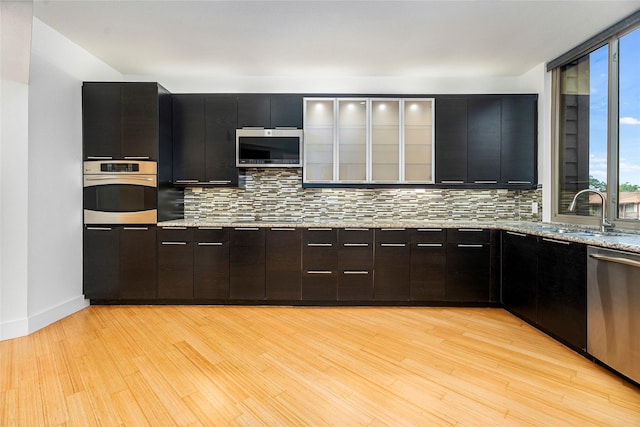 18405 Sandy Cv, Houston, TX 77058 - kitchen with stainless steel appliances, tasteful backsplash, light wood-type flooring, and glass insert cabinets
