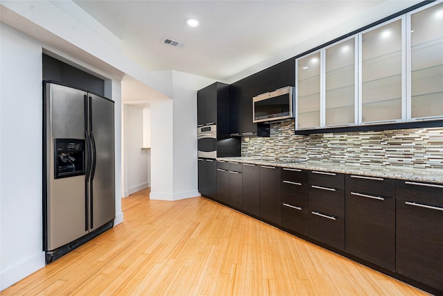 18405 Sandy Cv, Houston, TX 77058 - kitchen featuring appliances with stainless steel finishes, tasteful backsplash, light wood finished floors, glass insert cabinets, and recessed lighting