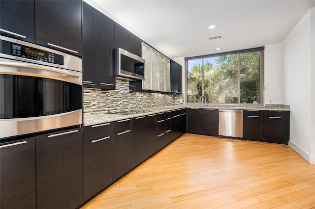 18405 Sandy Cv, Houston, TX 77058 - kitchen with appliances with stainless steel finishes, dark cabinetry, light wood-style floors, decorative backsplash, and recessed lighting