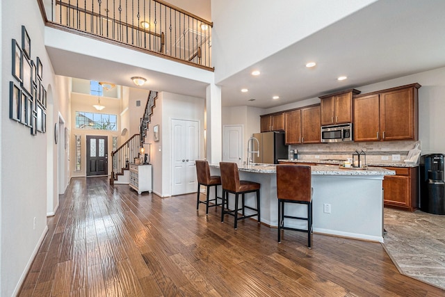 9215 Union Meadow Ln, Cypress, TX 77433 - kitchen featuring appliances with stainless steel finishes, a towering ceiling, dark wood-style flooring, a center island with sink, and decorative backsplash