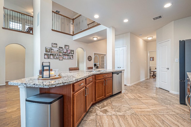 9215 Union Meadow Ln, Cypress, TX 77433 - kitchen with dishwasher, arched walkways, brown cabinetry, light stone counters, and an island with sink