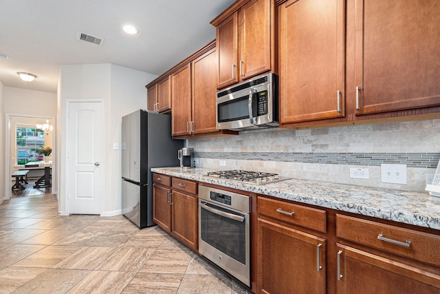 9215 Union Meadow Ln, Cypress, TX 77433 - kitchen featuring stainless steel appliances, brown cabinetry, decorative backsplash, and light stone countertops